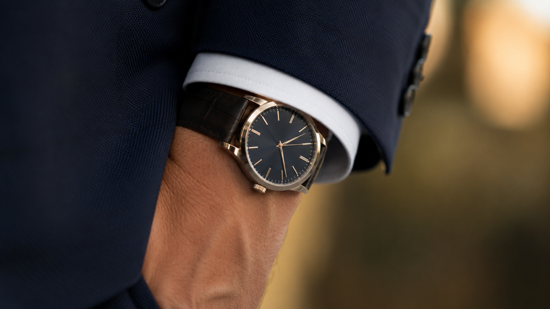 A close up lifestyle shot of a gold dress watch fitting elegantly under a suit cuff to show proper wrist proportions when considering what is watch case size